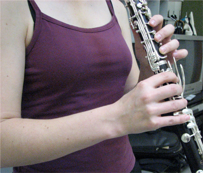 Henkilö soittaa klarinettia etuviistosta katsottuna. Yläraajat ja soitin.